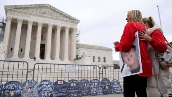 Two women stand outside the Supreme Court, wher<em></em>e signs in the shape of grave headstones, with information on people who died from using OxyContin, line a security fence, in Washington, Dec. 4, 2023.