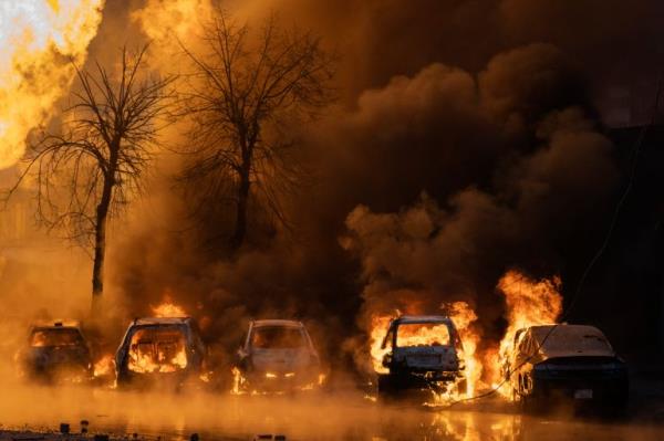 Cars on fire after a Russian drone and missile attack on Kyiv. The outlines of the cars can be seen through the intense orange flames. A tree is behind.