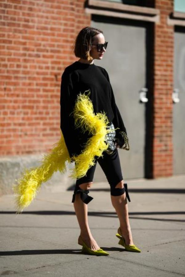 During NYFW, Katya Bychkova wears all black ensemble with gauchos tied in bows and yellow boa