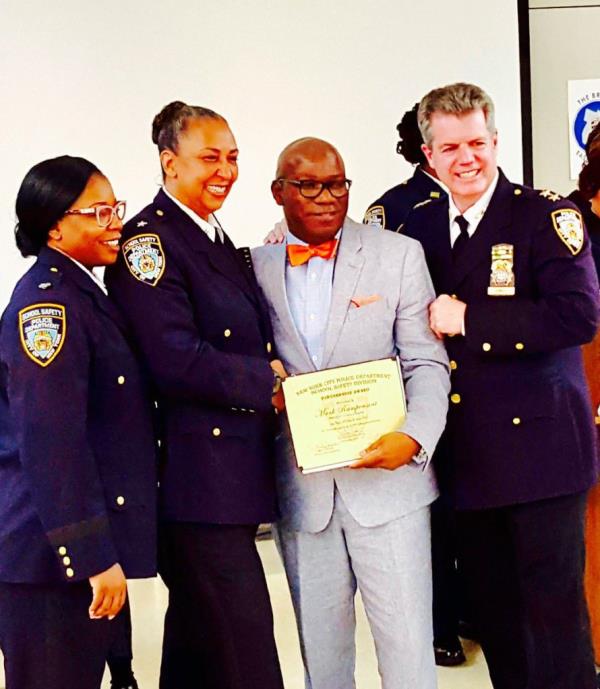 Mark Rampersant seen here in grey suit and orange bow tie, flanked by members of the nypd