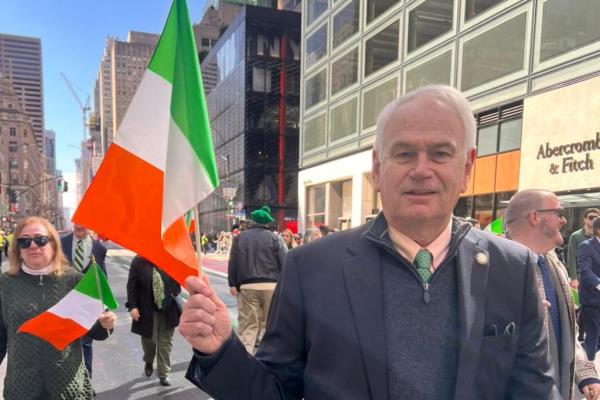 Queens Councilman Robert Holden looking into the camera while  holding an irish flag outside at a parade