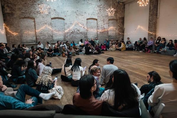 Matt Goldstein directing the Gaia Music Collective choir in a performance, with an audience of 180 people participating in singing along at a venue in the Gowanus area, Brooklyn, NY.