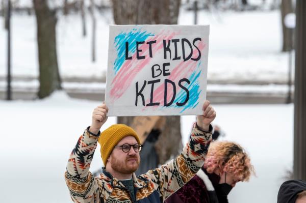 A man holding a sign at a rally in St. Paul, Minnesota, supporting transgender kids amid increasing attacks.