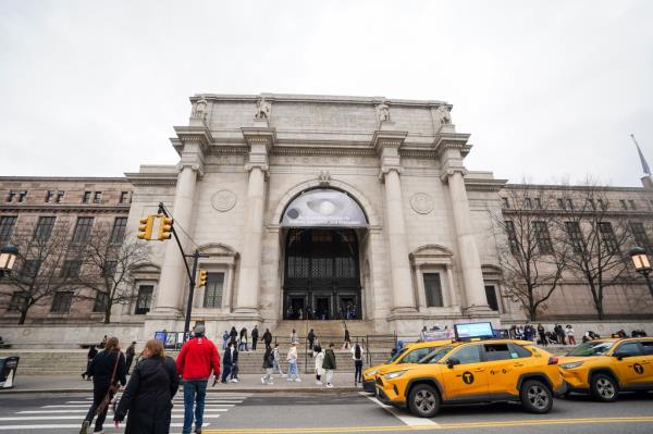 Outside of Museum of Natural History in Manhattan seen from outside with people crossing street and taxis waiting.