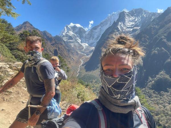 A family of three posing for a photo on the Everest trail, with a mountain in the background.