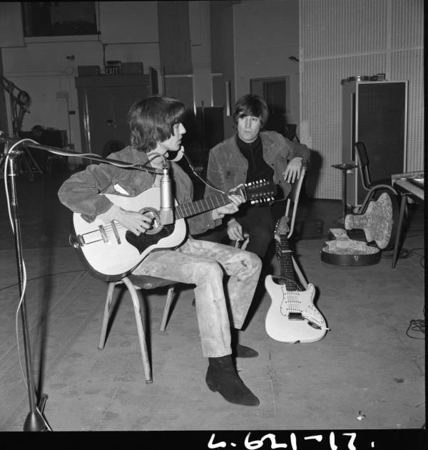 A photo of George Harrison playing the 12-string acoustic while John Lennon watches.