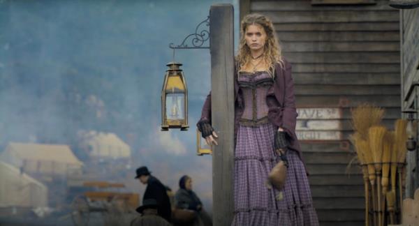 Abbey Lee standing by a house in a pio<em></em>neer dress. 