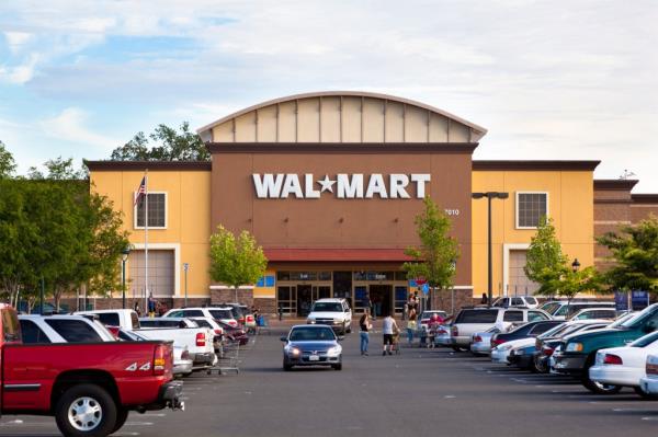 The outside of a Walmart store with parking lot and shoppers a<em></em>bout.