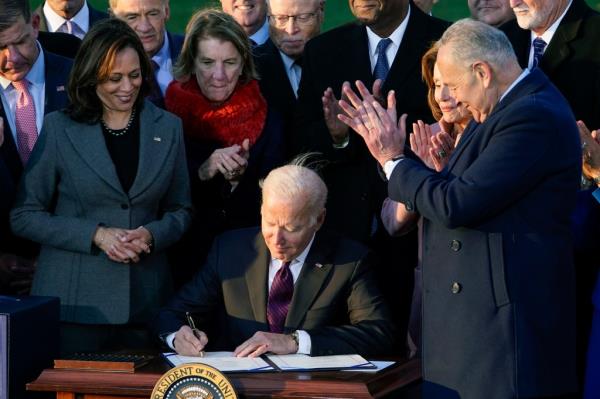 President Joe Biden signing the bipartisan infrastructure bill into law while surrounded by people on the White House lawn.