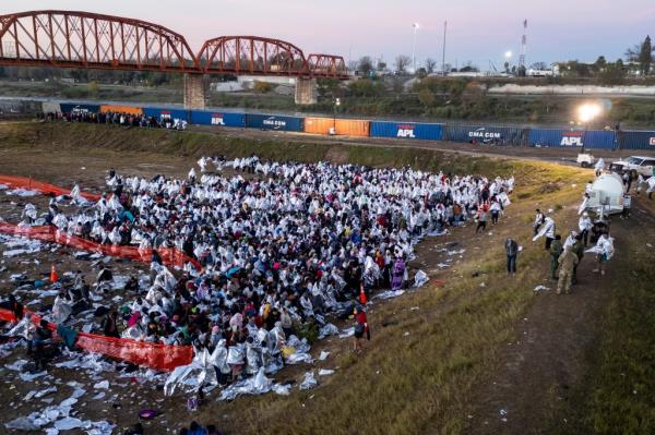 As seen from an aerial view immigrants, many wearing mylar blankets supplied by the U.S. Border Patrol, try to stay warm after spending the night outside a processing center next to the U.S.-Mexico border on December 18, 2023 in Eagle Pass, Texas