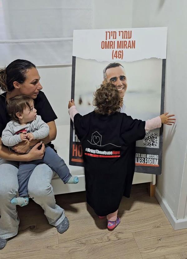 Roni, 2, hugs a poster of her father as heartbroken mother Lishay Lavi looks on with her toddler, Alma.