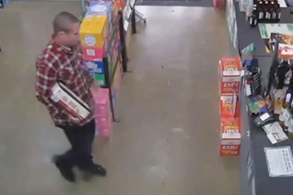 Man in red flannel carries a box of bottles inside liquor store. 