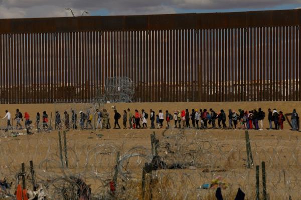 Migrants seeking asylum in the United States gather near the border wall after crossing a razor wire fence deployed to inhibit their crossing into the United States, while members of the Texas Natio<em></em>nal Guard stand guard, as seen from Ciudad Juarez, Mexico January 22, 2024. 