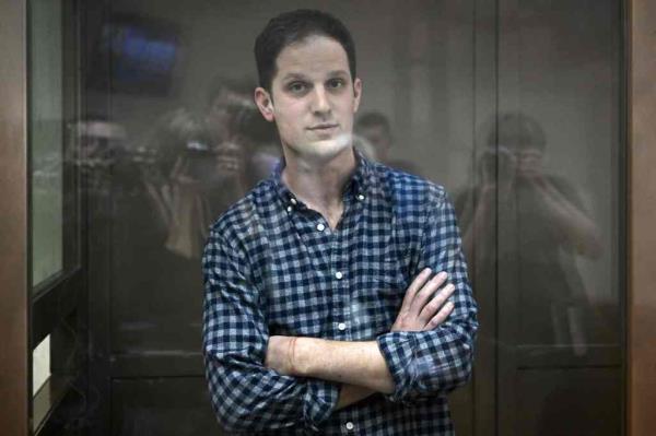 evan gershkovich folds his arms from behind a protective transparent shield in a courtroom