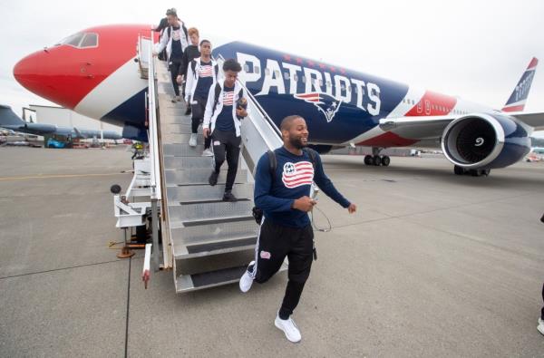 Patriots players coming down stairs off branded airplane.