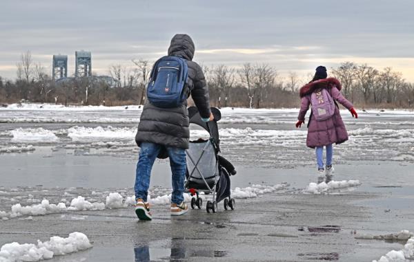 Migrants walking and pushing a stroller on snow-covered ground at Floyd Bennett Field in Brooklyn, NY.