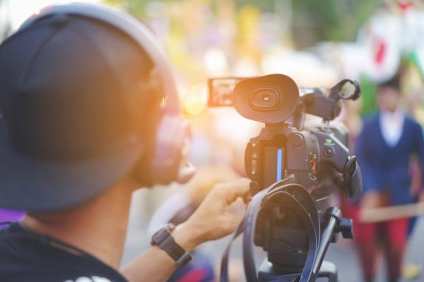 Videographer Christian Jo<em></em>nes using professio<em></em>nal video camera with Wi-Fi transmitting device, headphones, and outdoor setup for live stream production.