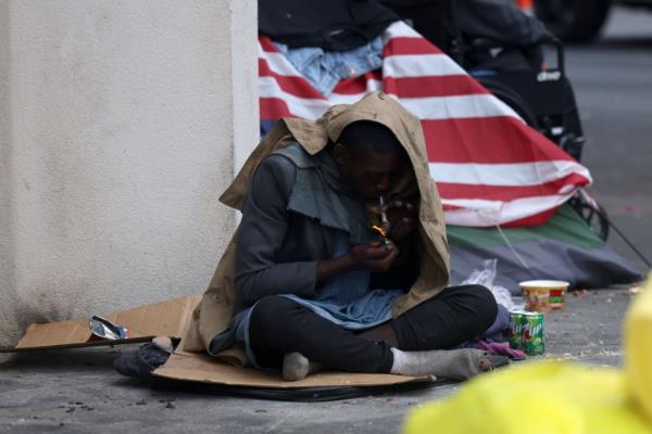 A man smokes drugs on a sidewalk in Skid Row.