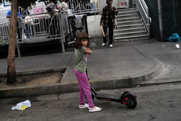 A child plays on the street near homeless people smoking and injecting drugs on Skid Row.