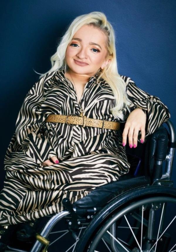 Samantha Renke in her wheelchair, wearing a zebra print dress, in front of a dark blue wall