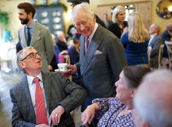 King Charles III, holding a cup and saucer, reacts as he meets with guests during a 75th birthday party for him, hosted by the Prince's Foundation at Highgrove House.