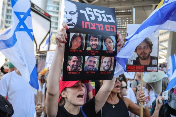 A woman holds up a sign with pictures of the six israeli hostages found dead in Gaza this week. She's at a protest surrounded by people waving